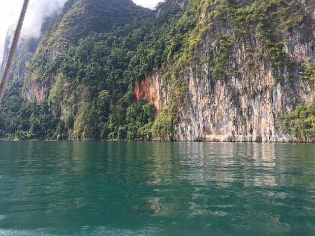 Beautiful limestone cliffs with green foliage by a water body.
