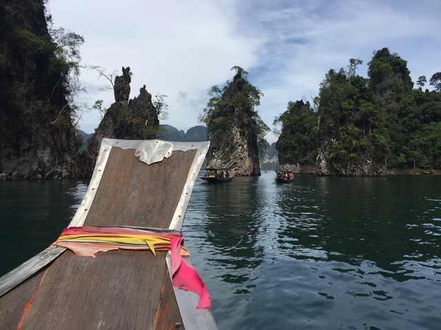 Longtail boat heading toward towering rocks on a lake.