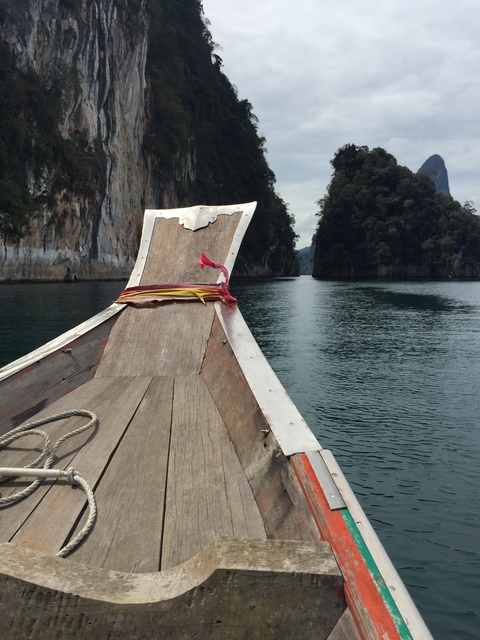 Wooden boat heading between tall cliffs on water.
