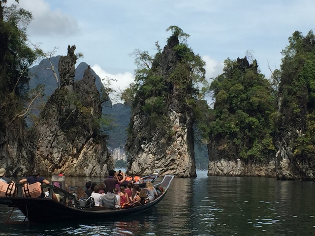 Tourists on boats approaching towering limestone formations.