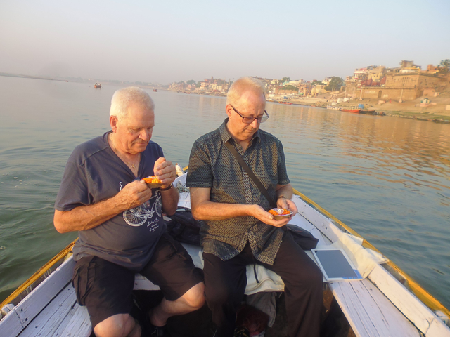 Two men on a boat performing a ritual in Varanasi.