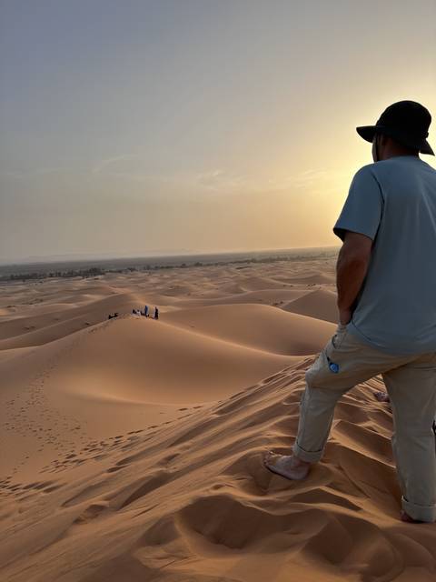 People standing on sand dunes during sunset.