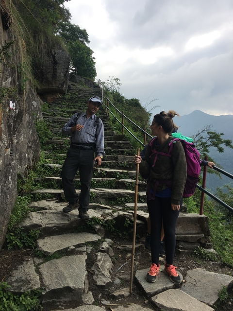 Two hikers talking on stone steps surrounded by greenery and mountains.