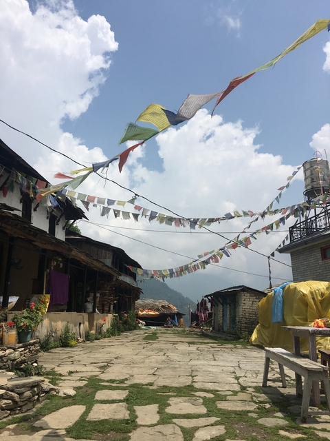 Tibetan prayer flags hanging between buildings with a mountain backdrop.