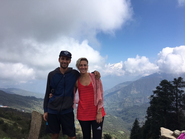 Two people posing in front of a mountainous landscape with clouds in the sky.
