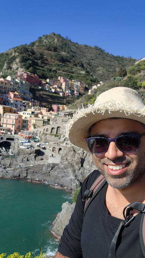 Selfie of a person with a view of a colorful cliffside town and sea behind.