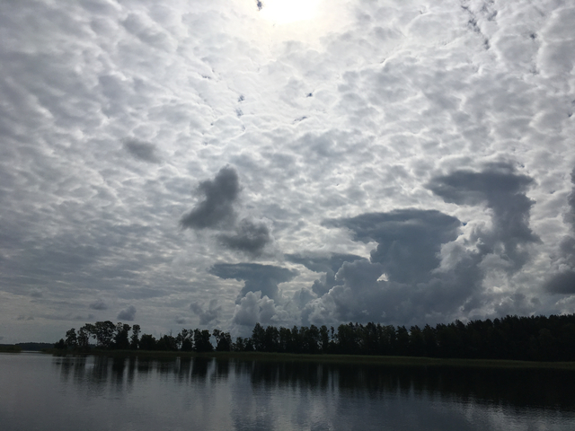 Dark cloudy sky over still water, reflecting trees.