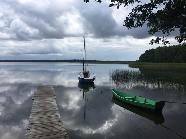 Small boats docked at a tranquil lake with cloudy sky.