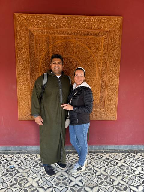 Two people posing in front of an intricately carved wall.