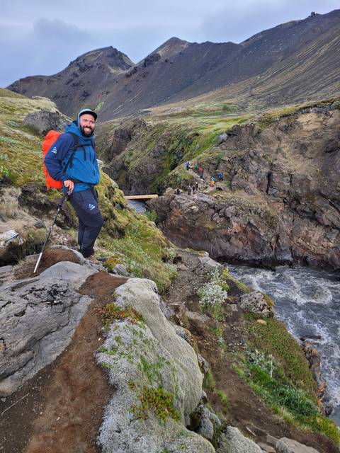 Hiker in volcanic landscape with a river and bridge in the background.