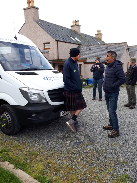 Tour group by a van, one person in a kilt.