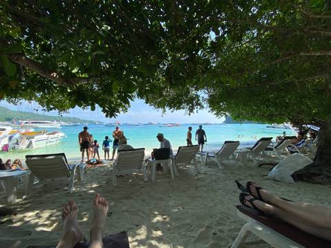 Busy beach scene with people and boats on the water.