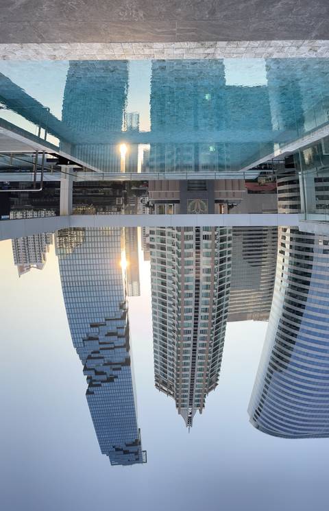Skyscrapers reflected in a pool with a cityscape background.
