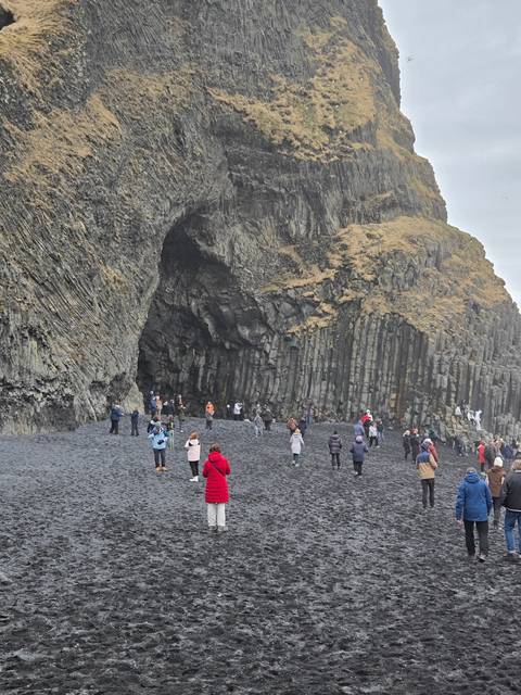 People exploring a black sand beach with unique rock formations.
