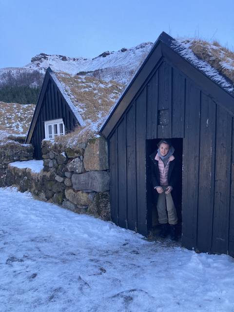 Small house in snowy surroundings with a person standing at the doorway.