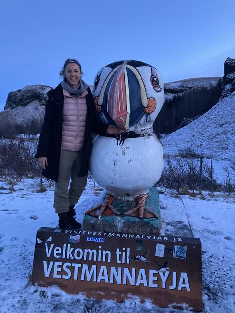 Person posing with a large bird sculpture, snow-covered landscape.