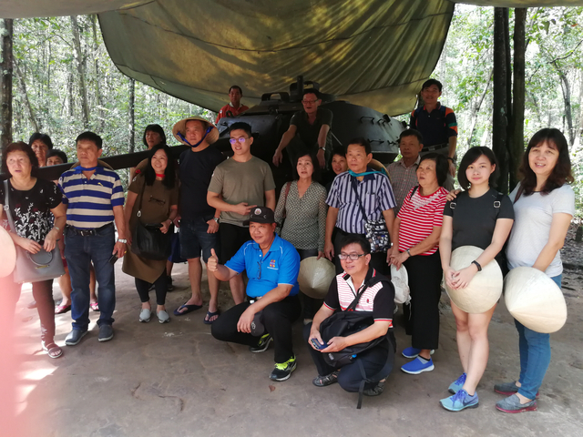 Group of people posing in front of a military tank.