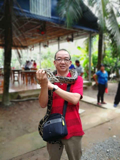 Man holding a snake, with people in the background.