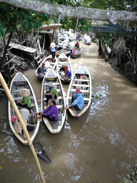 People paddling on small wooden boats in a muddy river.