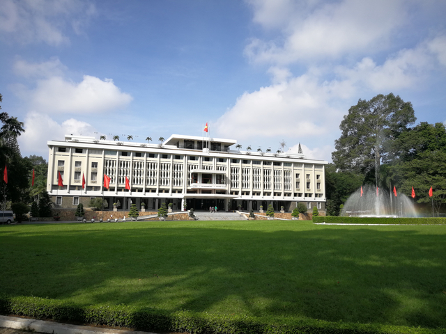 Grand government building with flags and a fountain.