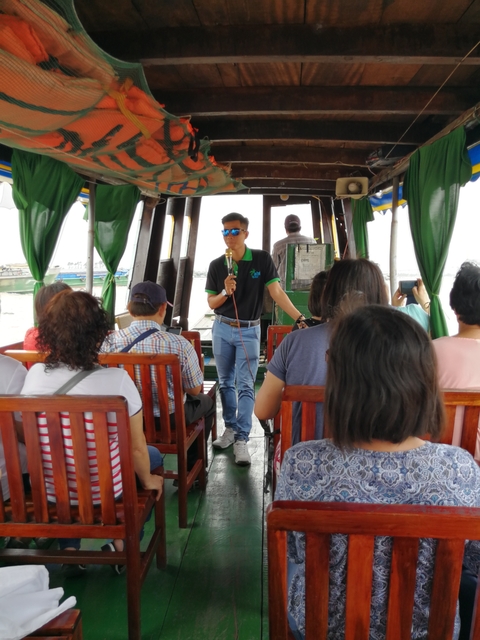 Group of people sitting on a boat with a guide speaking.