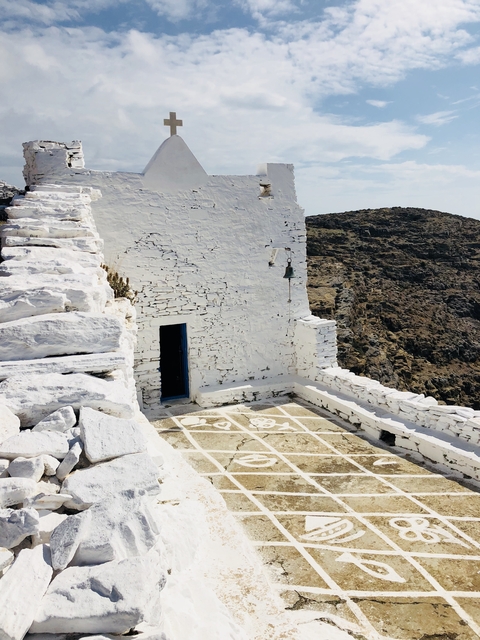 White stone wall with a small door and bell, located on a rocky landscape.