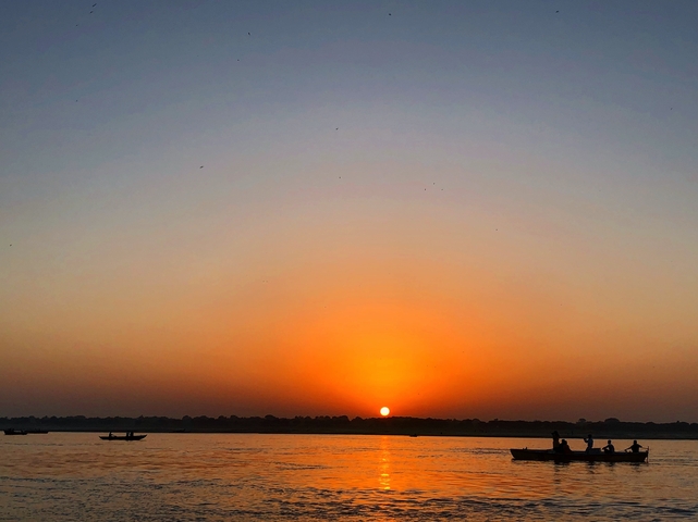 A beautiful sunset over a calm river with boats in the background.