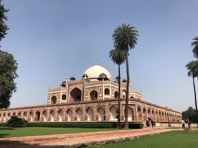 A grand structure with a dome and arches in a landscaped garden.