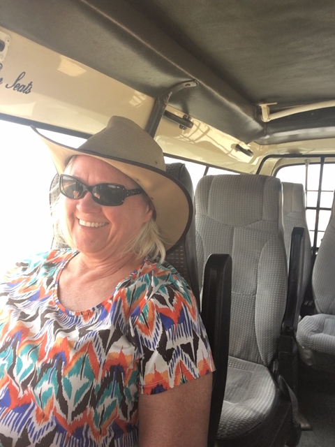 A woman smiling inside a vehicle, wearing a hat and sunglasses.