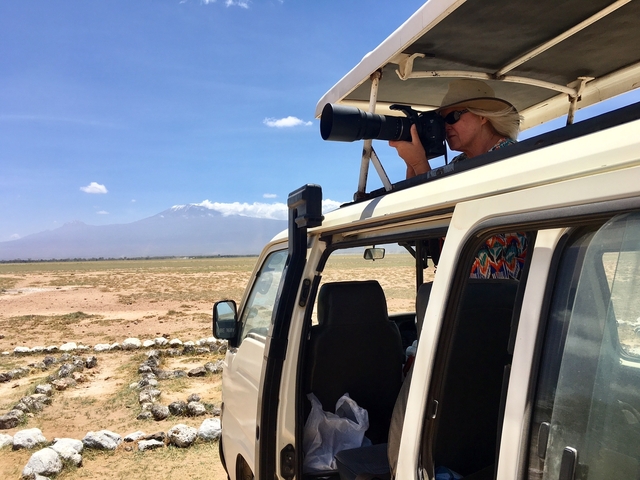A person photographing a distant mountain from a safari vehicle.