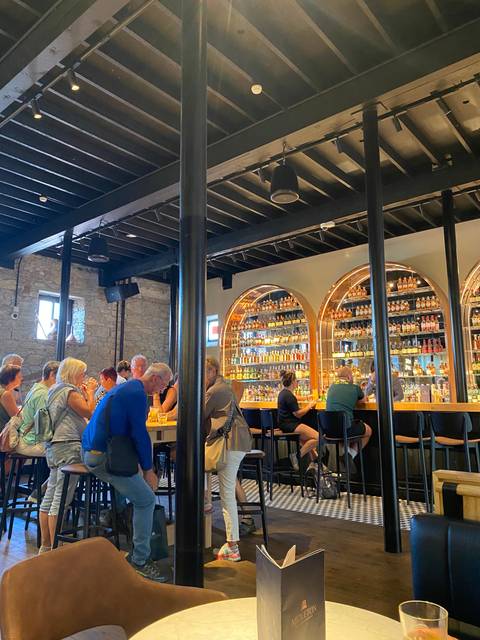 Interior of a bar with people seated at tables and illuminated liquor bottles.