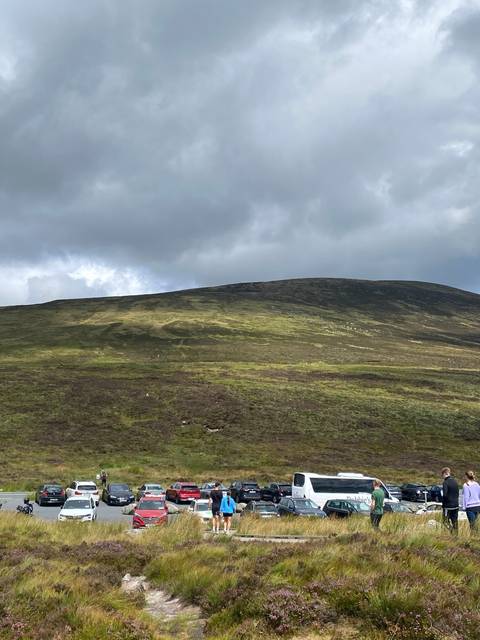 Hilly landscape with parked cars and people.