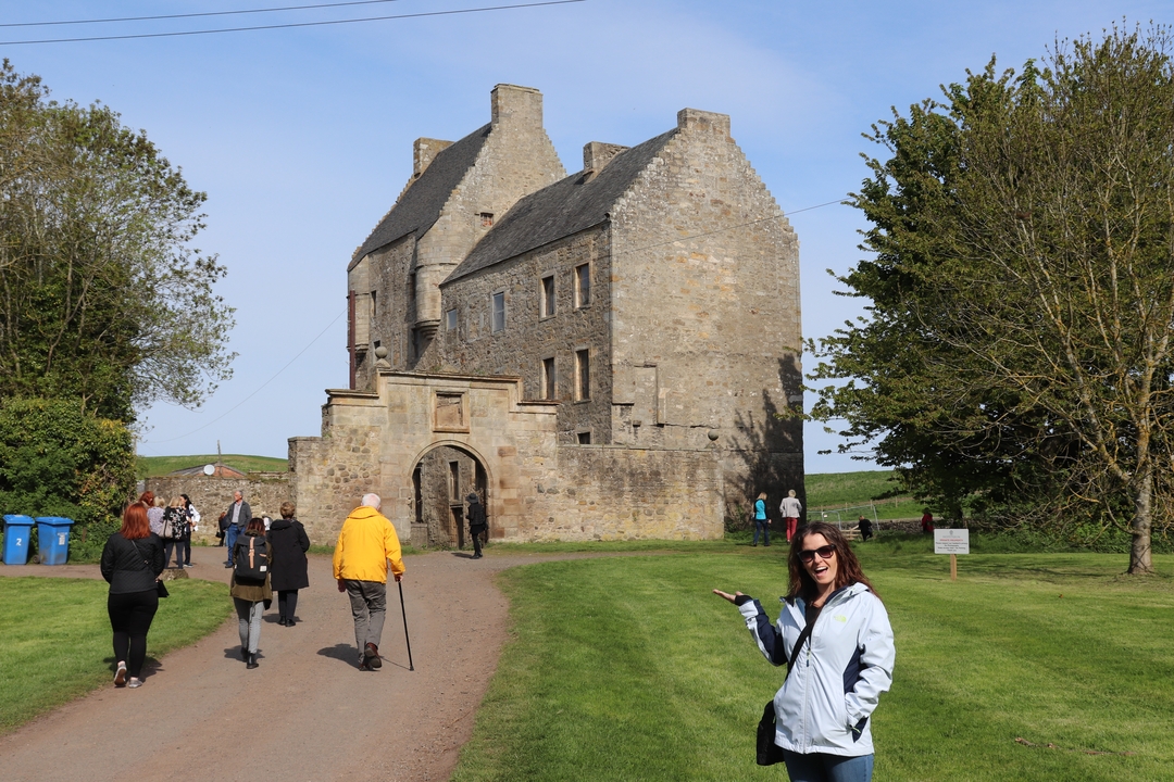 Des personnes visitent un château historique en pierre avec des arbres.