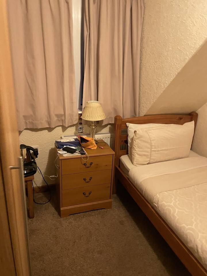 Coin de chambre simple avec une table de chevet et une lampe.