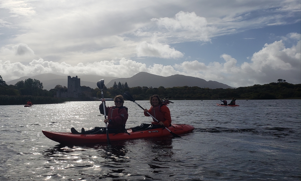 Deux femmes faisant du kayak sur un lac avec un château en arrière-plan.