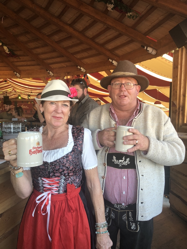Deux personnes en tenue bavaroise traditionnelle tenant des chopes de bière, dans un cadre festif.