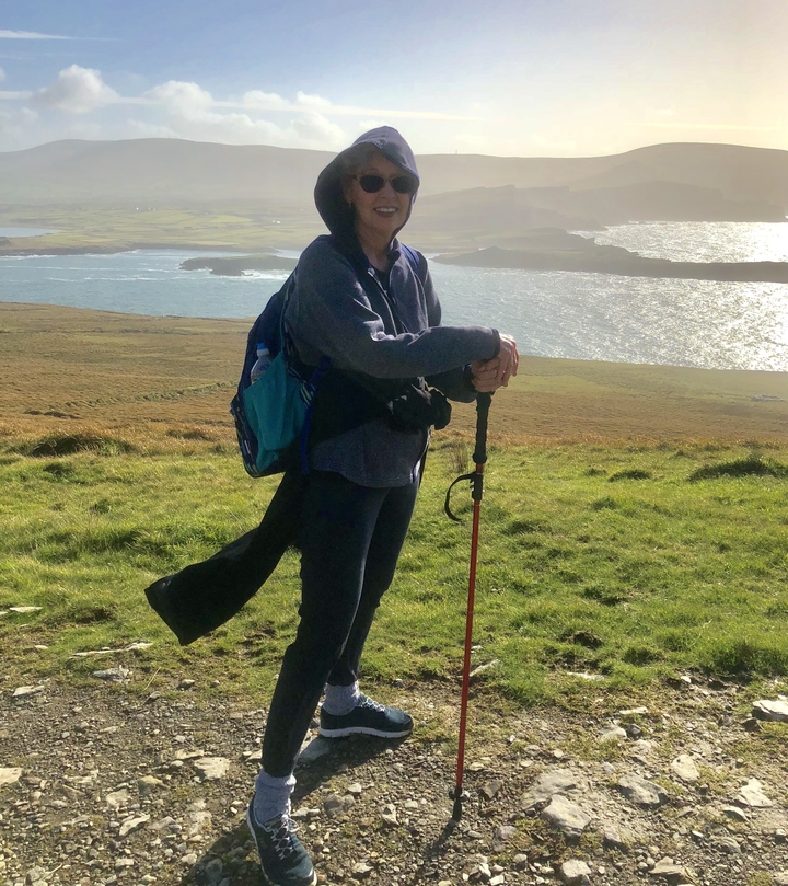 Hiker with trekking poles in a grassy area overlooking the ocean.