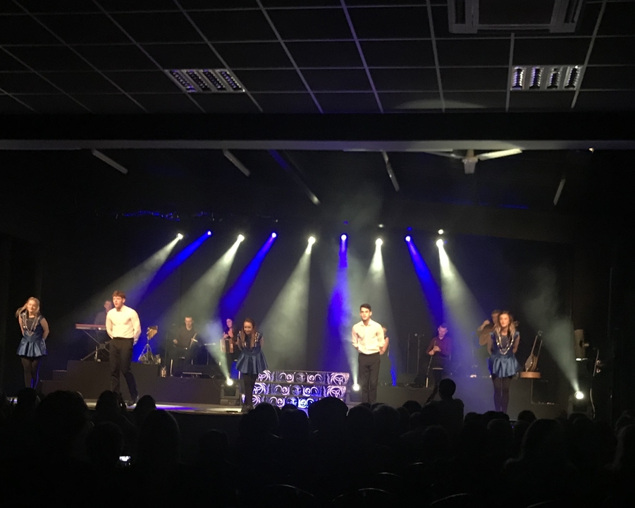 Spectacle sur scène avec un groupe de personnes dansant sous des éclairages bleus.