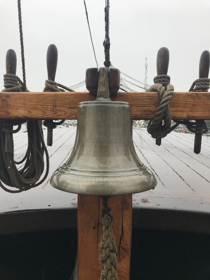 Une cloche de navire sur une structure en bois avec des cordes.