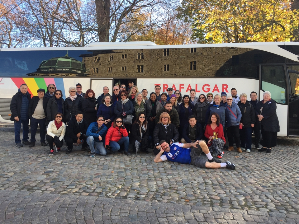Groupe de touristes posant devant un bus avec le reflet du bâtiment.