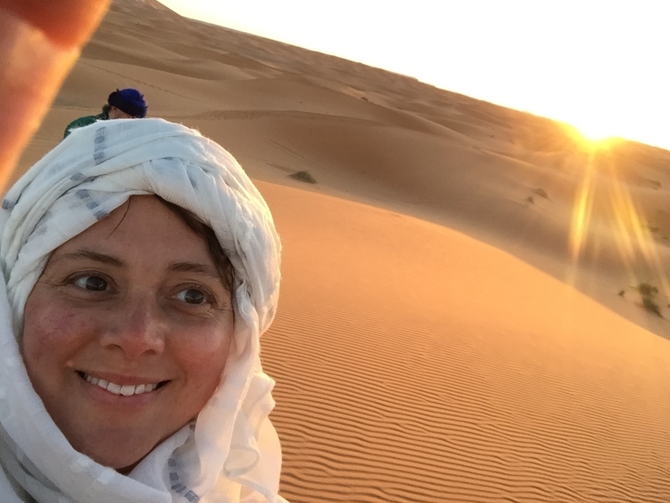 Personne en tenue traditionnelle avec des dunes du désert au coucher du soleil.