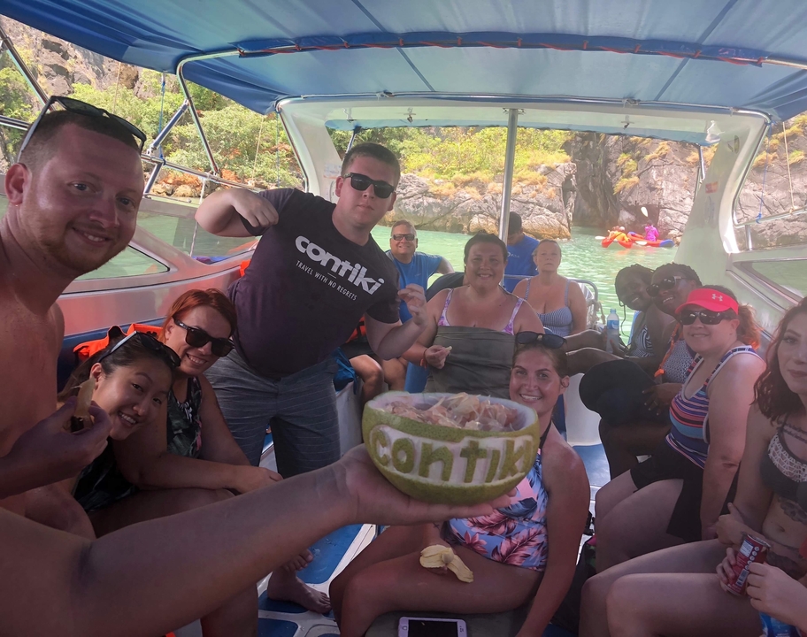 Touristes posant sur un bateau avec une noix de coco affichant 'Contiki'.