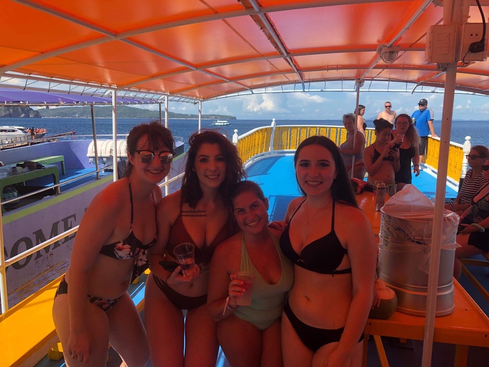 Groupe de femmes sur un bateau souriantes et tenant des boissons.
