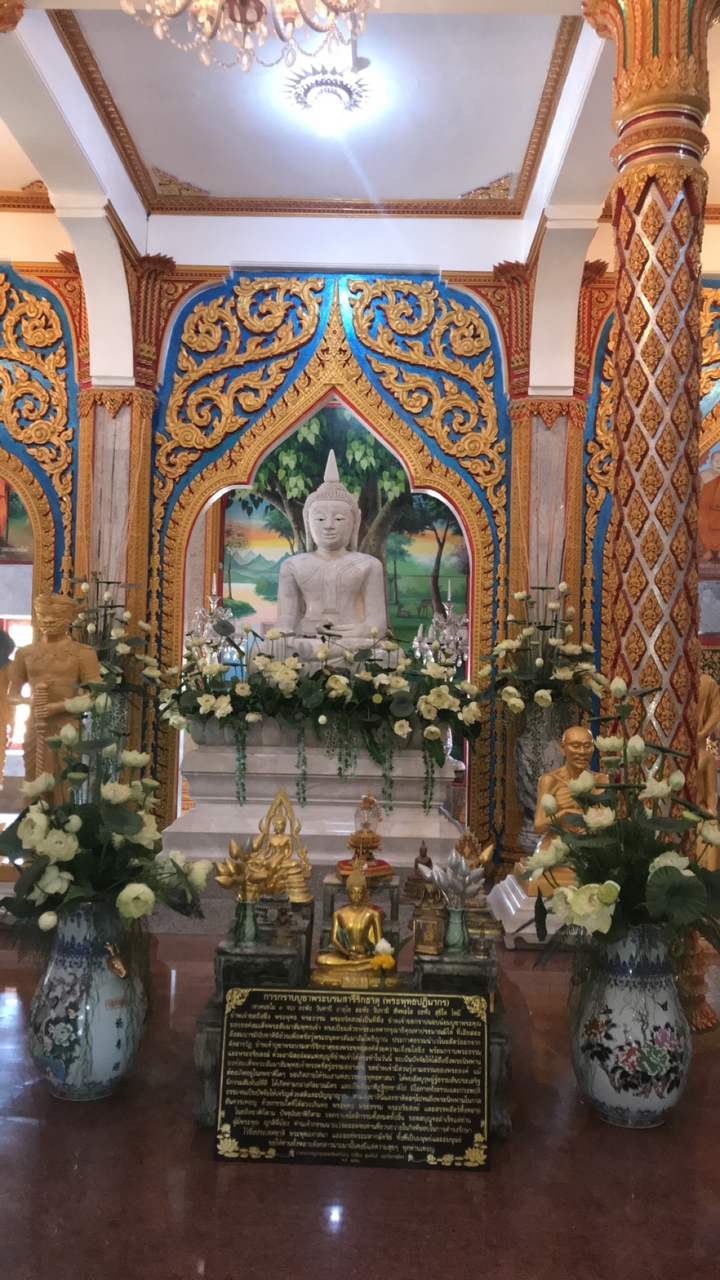 Statue de Bouddha en pierre blanche entourée de fleurs et d'offrandes.