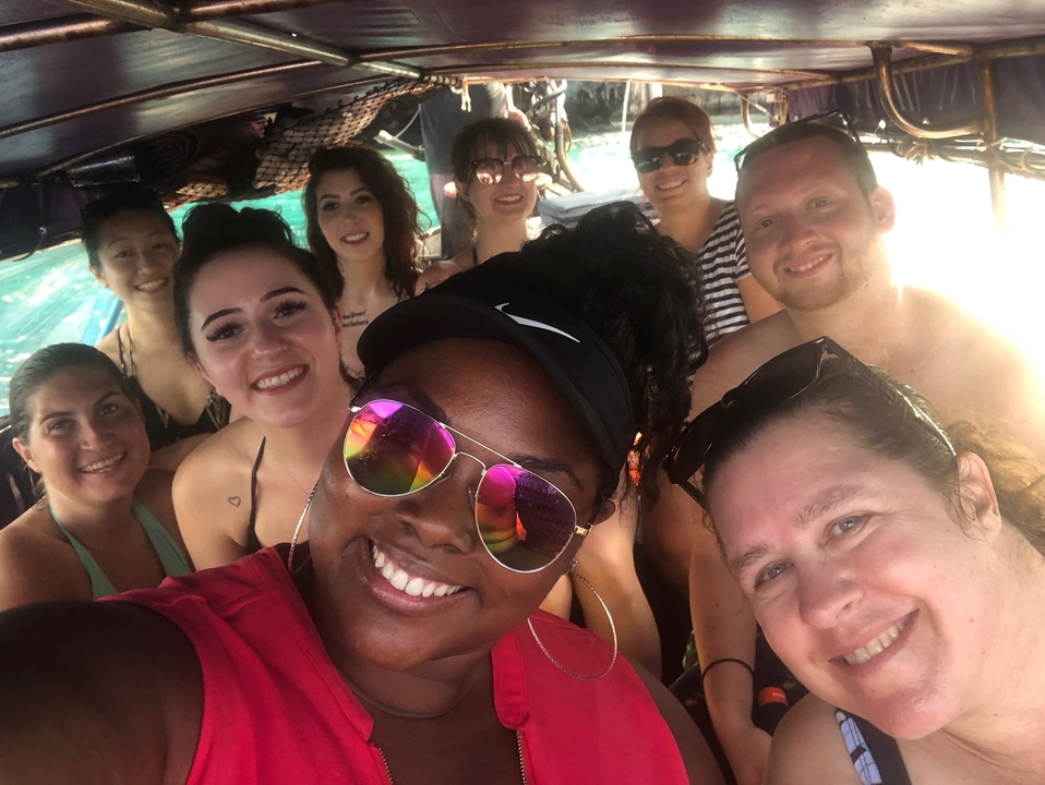 Groupe d'amis souriants sur un bateau avec de l'eau en arrière-plan.