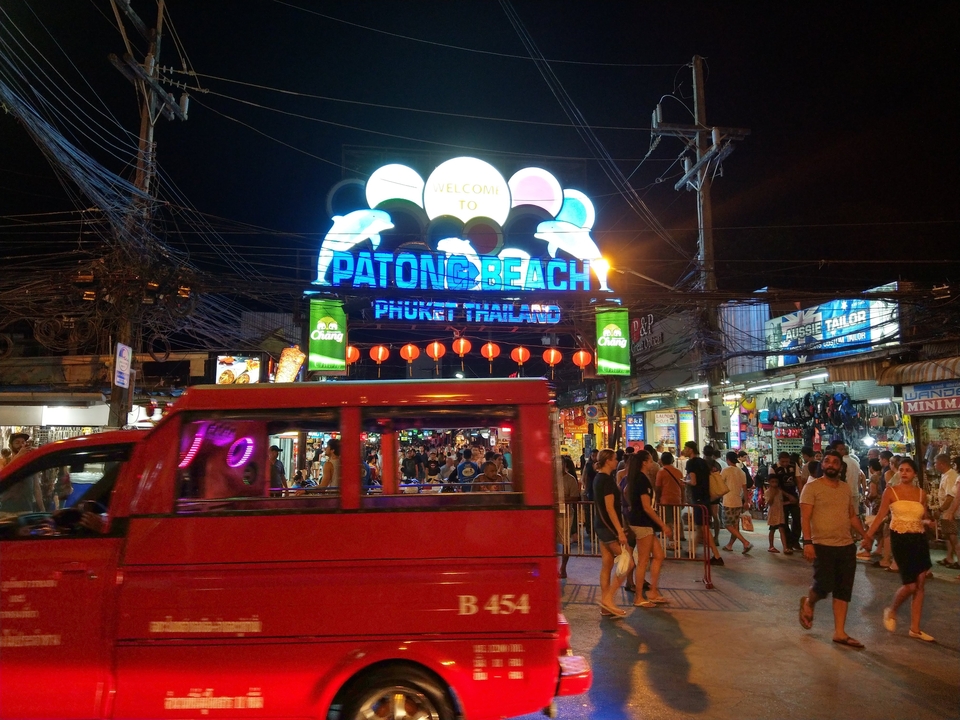 Scène animée de marché nocturne avec l'enseigne 'Patong Beach' illuminée.