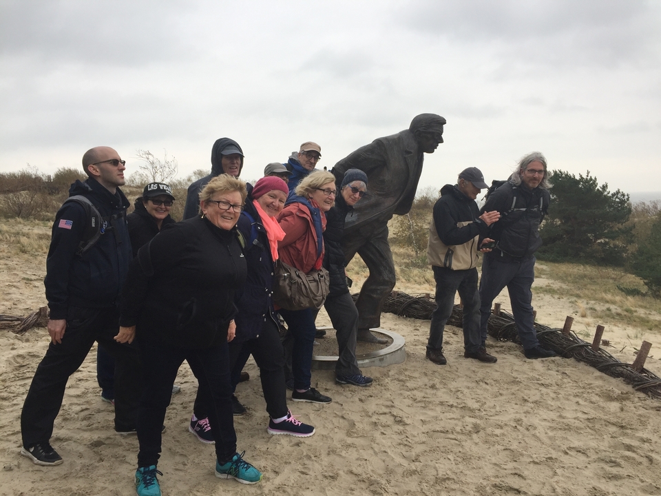 Des touristes qui posent avec une statue dans une zone sableuse et venteuse.