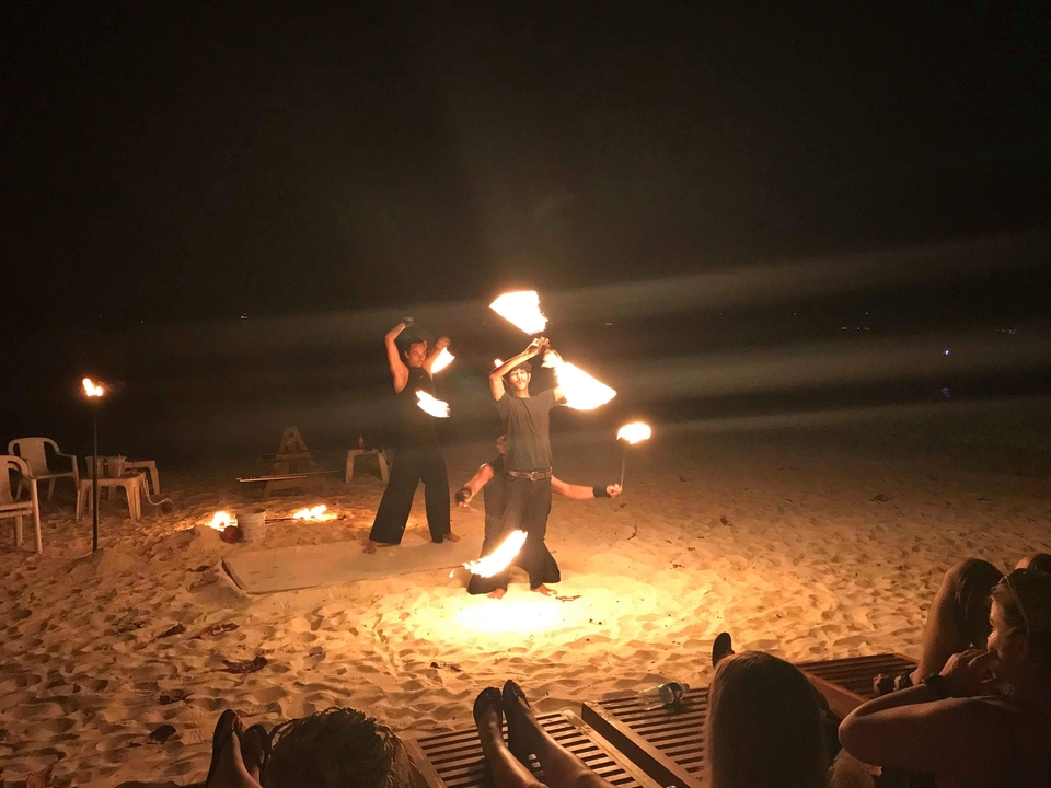 Artistes de feu la nuit sur une plage, entourés de sable et de chaises.