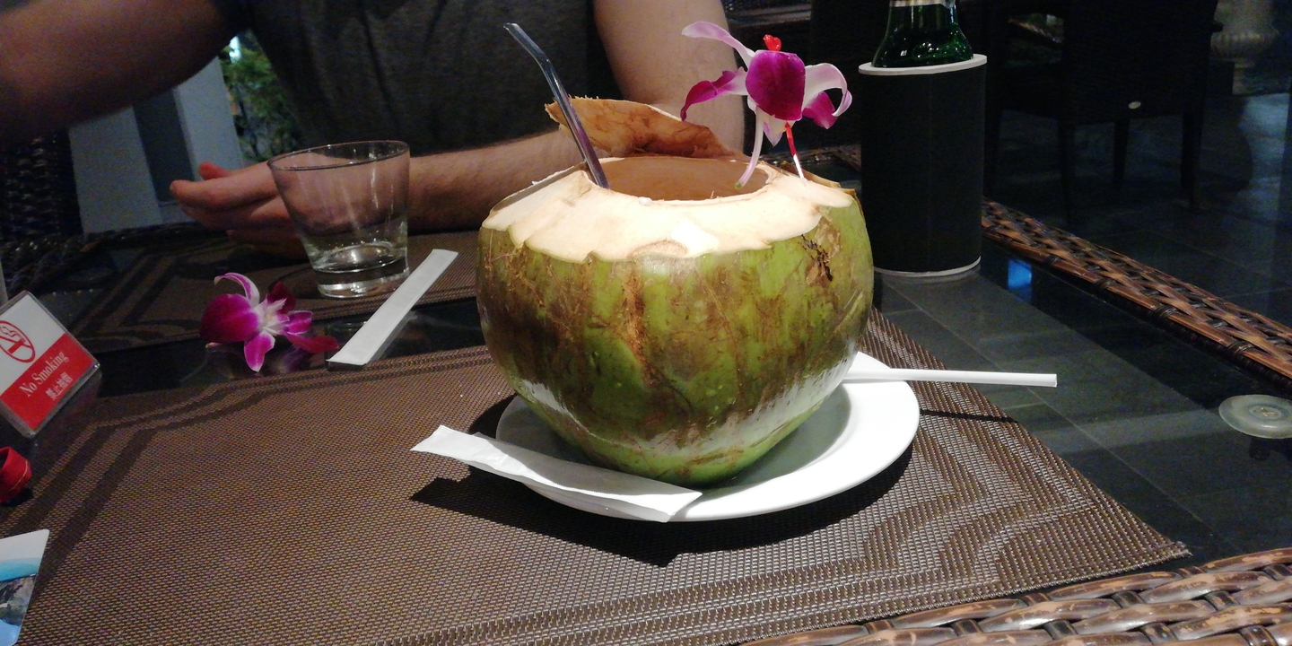 Table avec une boisson à la noix de coco et des fleurs, à l'intérieur sur un set de table.