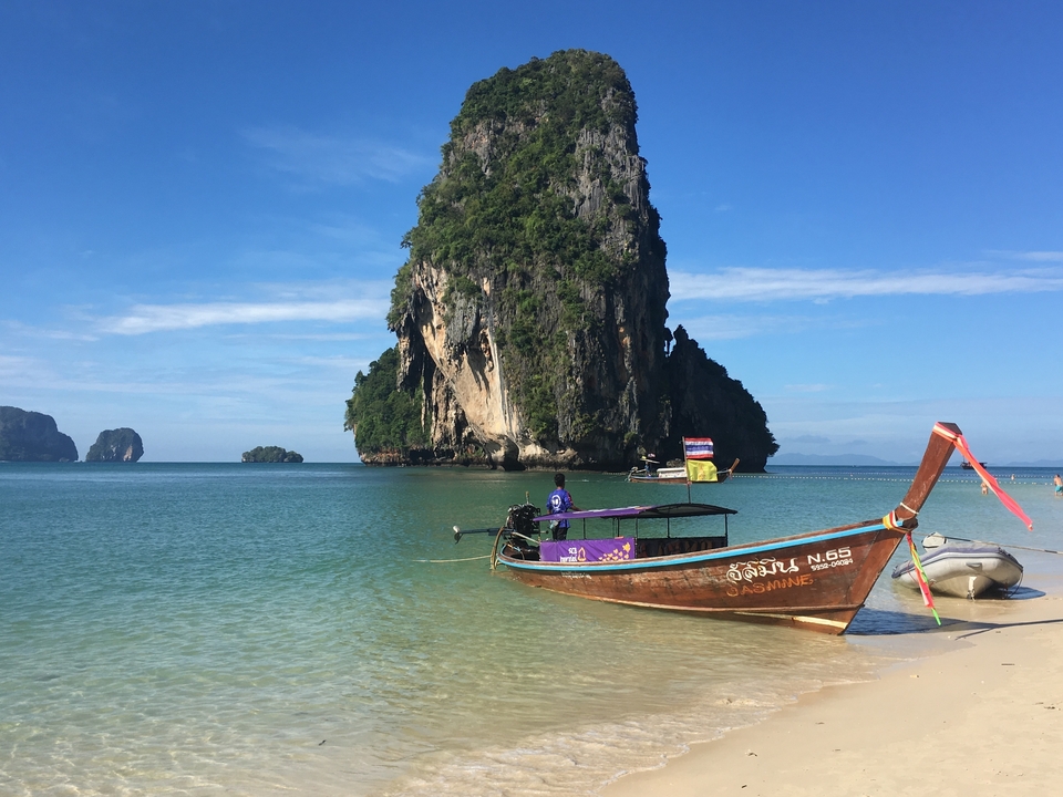 Bateau à longue queue traditionnel sur une plage tropicale avec une eau claire et des falaises calcaires.